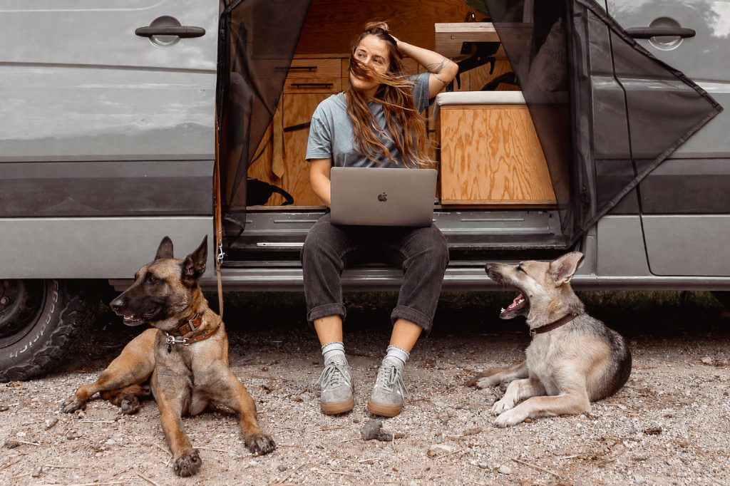 Helene Schütz sitzt an ihrem Van mit ihren zwei Hunden und einem Laptop auf dem Schoß.